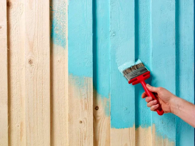 Photo of a hand holding a paintbrush putting a color light blue on a fence.